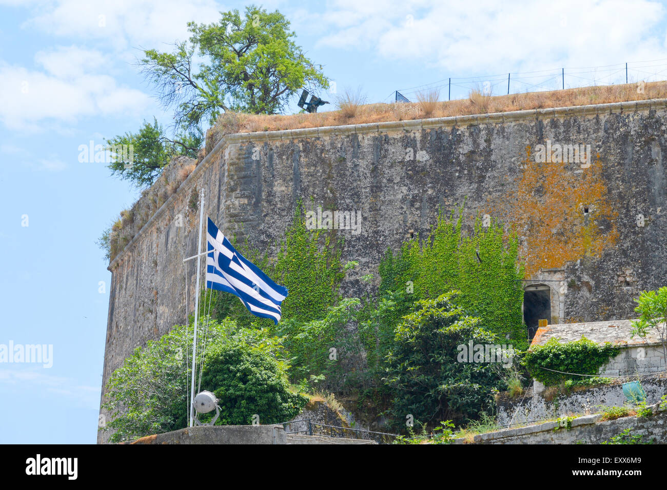 Waving flag of Greece in front of medieval fortress wall against cloudy blue sky Stock Photo