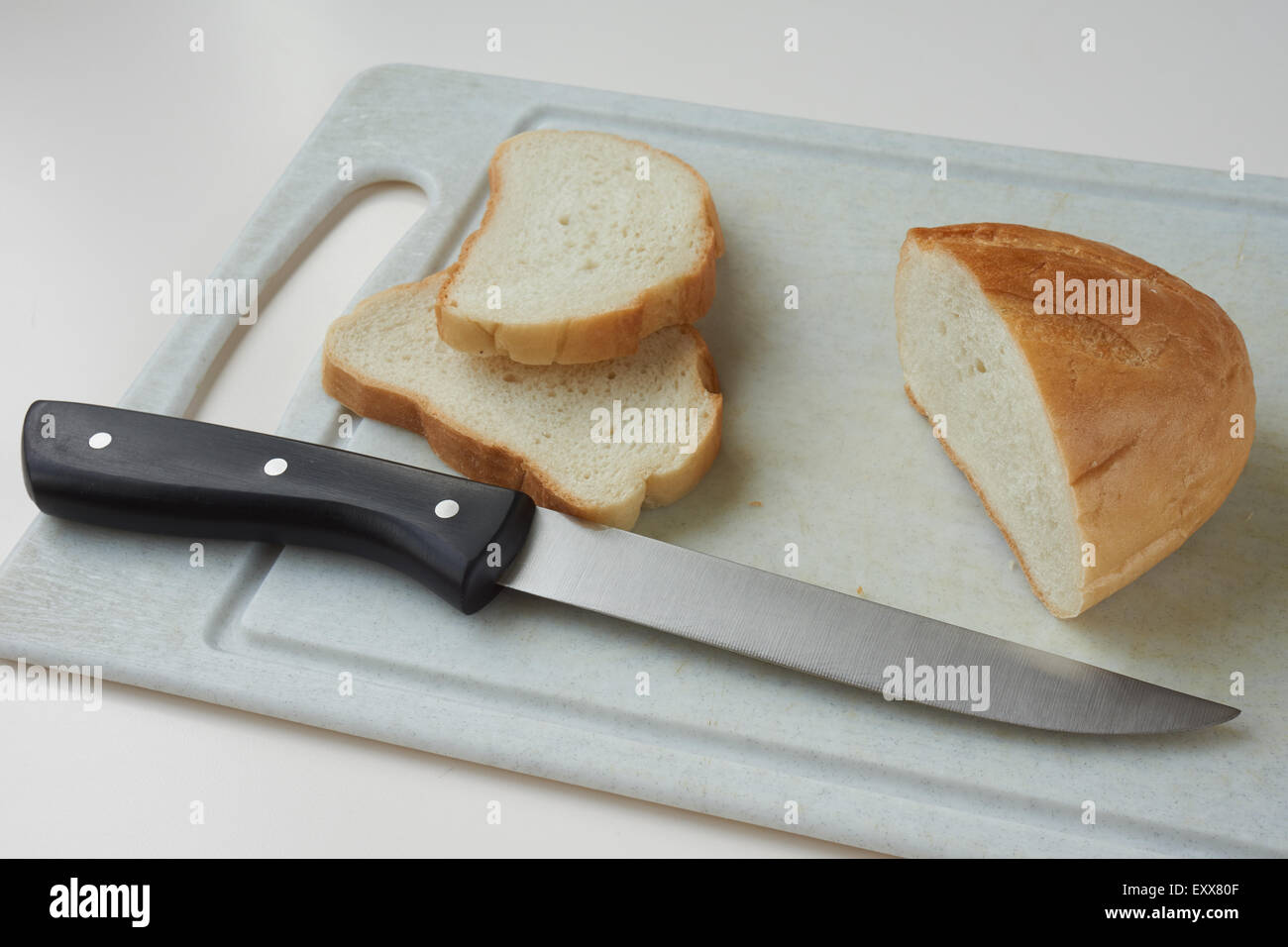 Still life with one knife, bread and two cut slices of bread on plastic cutting board Stock Photo