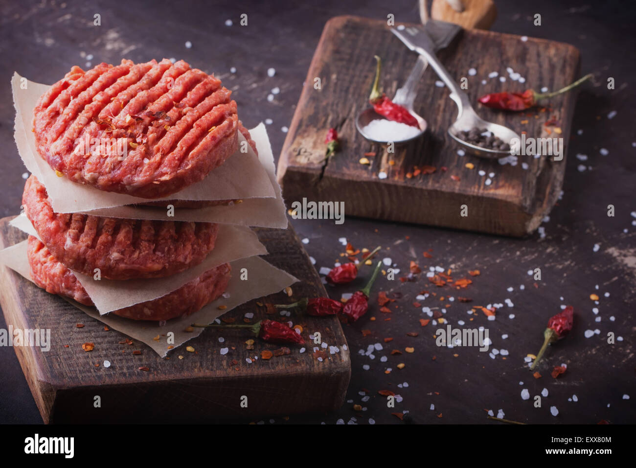 Raw Ground beef meat Burger steak cutlets with seasoning on vintage wooden boards, black background Stock Photo