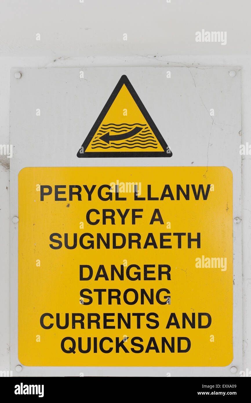 Information sign warning the public of strong currents and quicksand on the beach in welsh Stock Photo