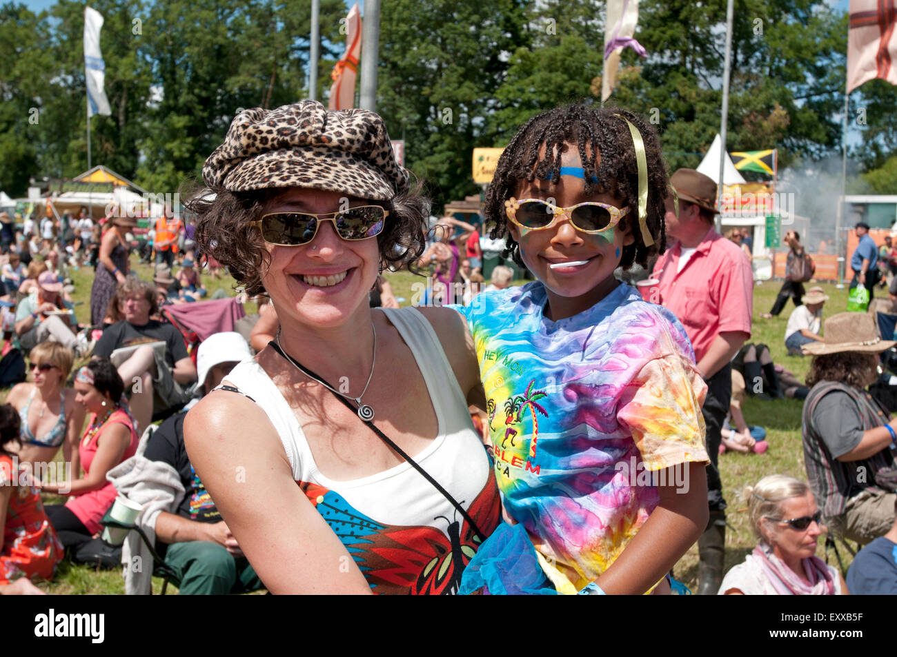A trendy mother holding her young child dressed in colourful festival clothes in the crowds at the WOMAD world music festival Stock Photo