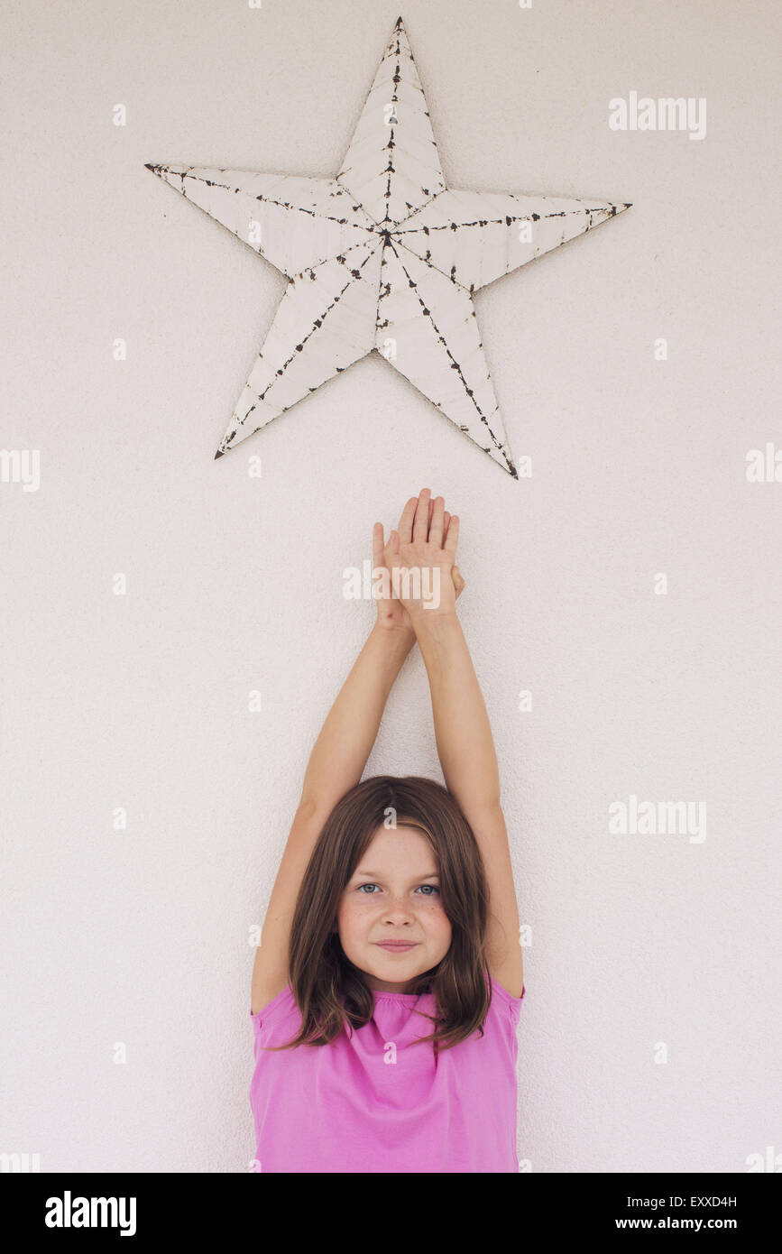 Girl reaching toward star shape hanging above her head, portrait Stock Photo