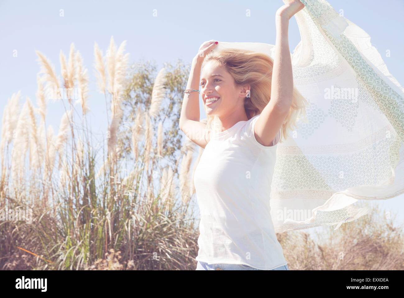Woman holding up scarf fluttering in wind Stock Photo