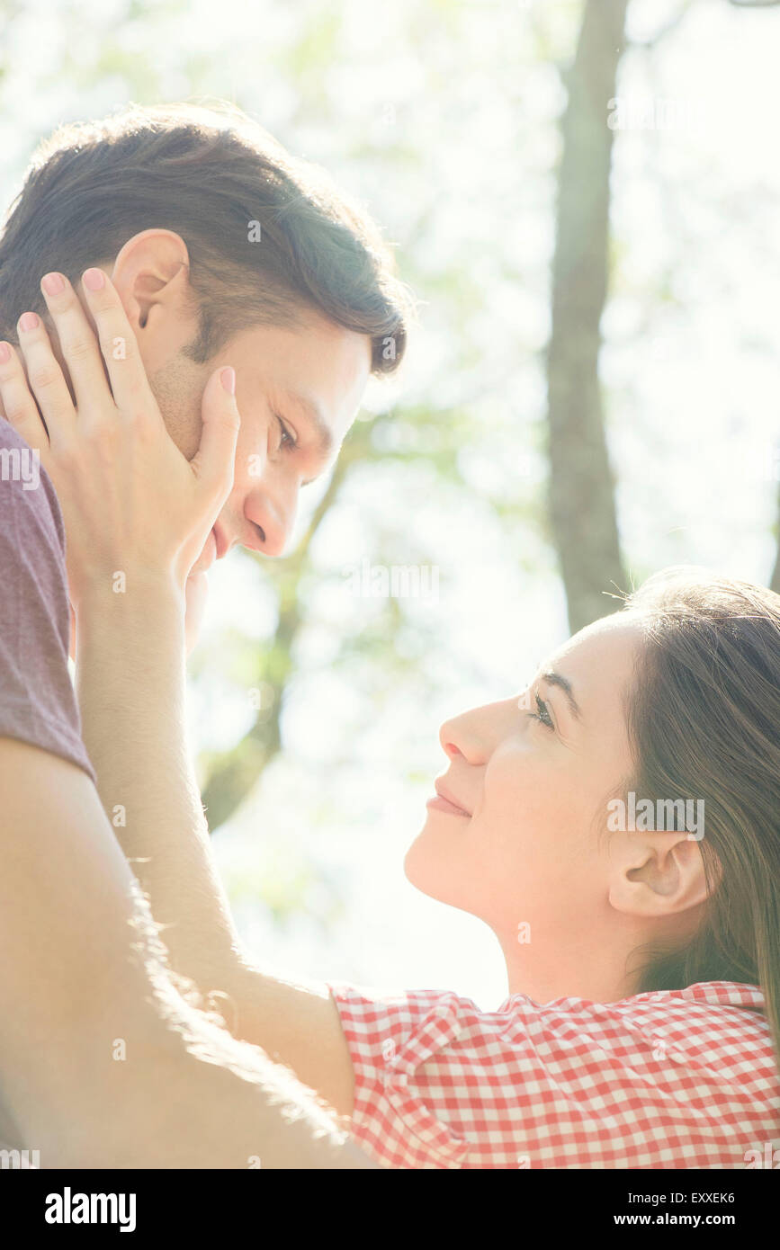 Couple together outdoors, woman holding man's face in her hands Stock Photo