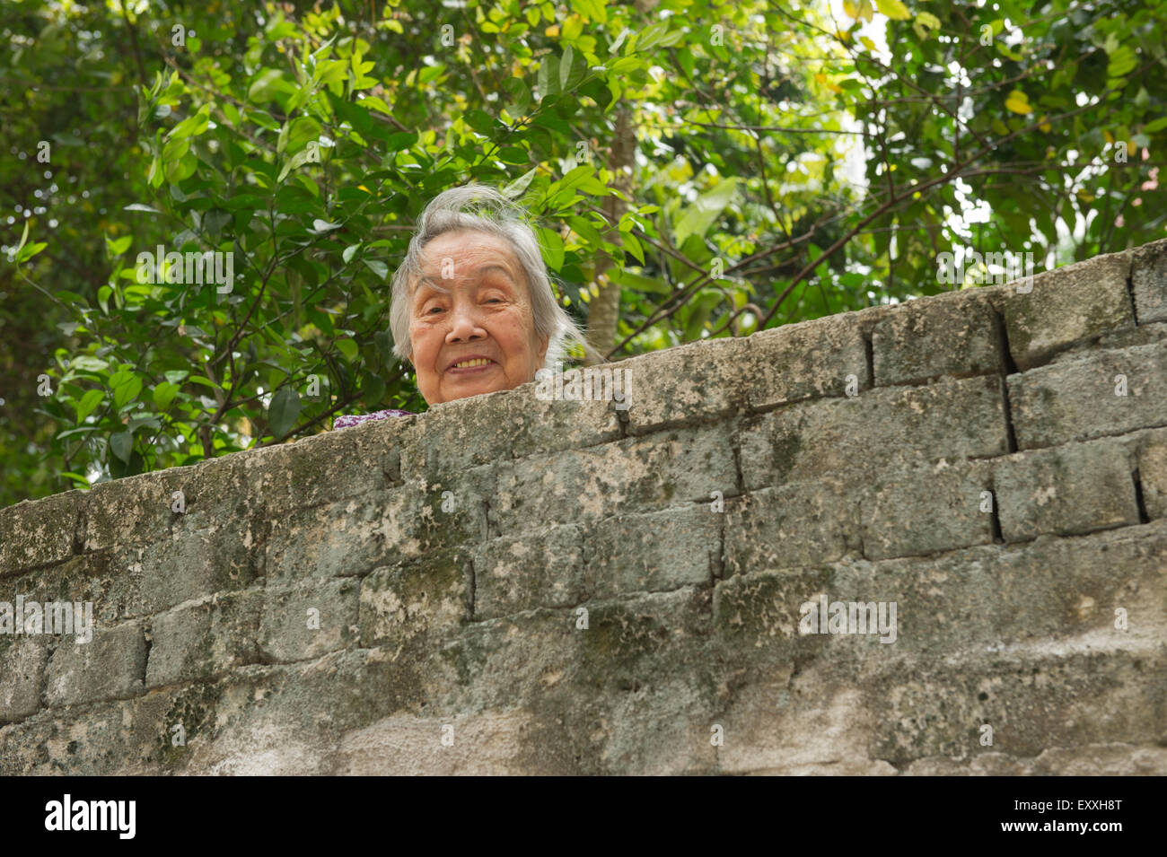 Elderly Asian lady looking over brick wall, Hong Kong, China. Stock Photo