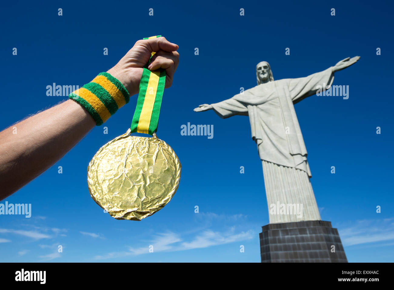 RIO DE JANEIRO, BRAZIL - MARCH 05, 2015: Hand holds gold medal hanging from Brazil color ribbons in clear blue sky at Corcovado. Stock Photo