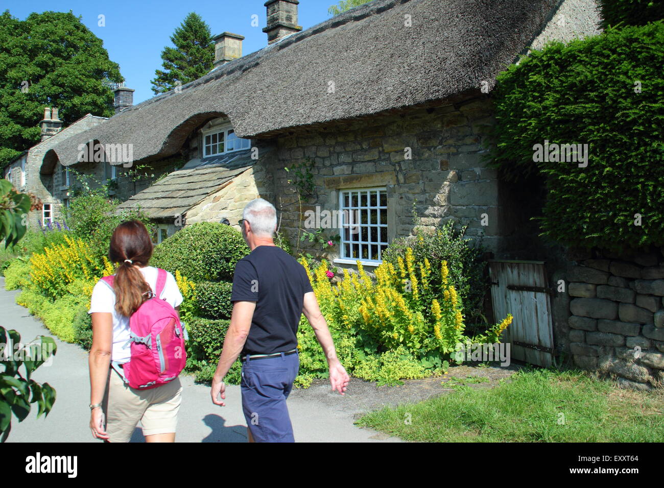 A man and woman walk by a traditional English thatched cottage in Baslow in the Peak District National Park, Derbyshire , UK Stock Photo