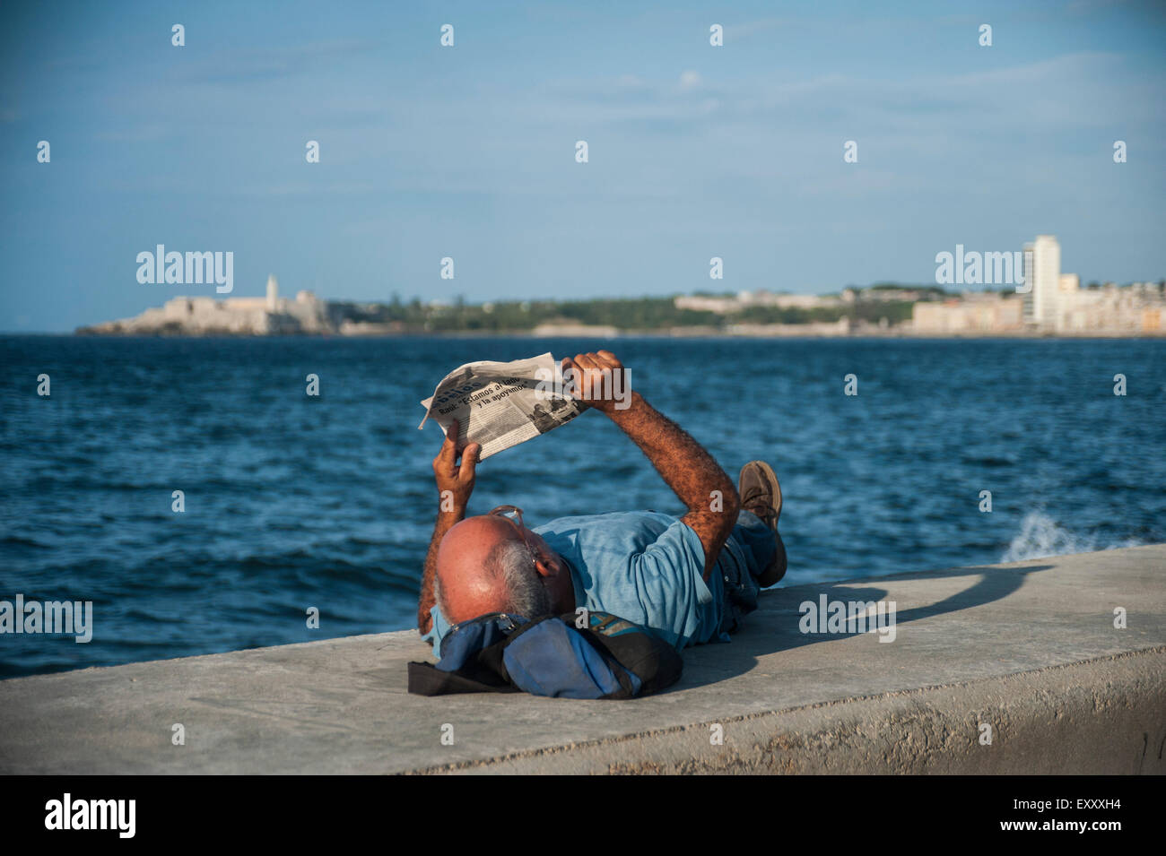 A man reads the newspaper and relaxes along the seawall and Malecon in Havana, Cuba Stock Photo