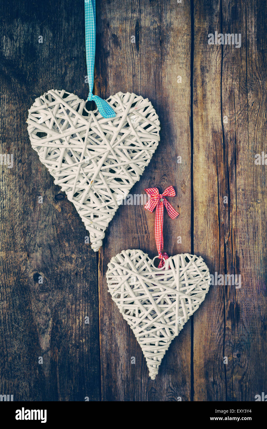 Two wicker hearts hanging on old wooden wall. Retro stylized. Stock Photo