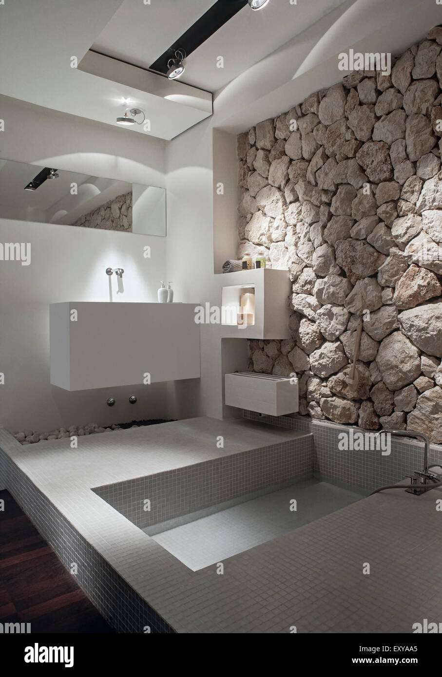 foreground of bathtub overlooking on washbasin in a modern bathroom whose wall is coated with stone Stock Photo