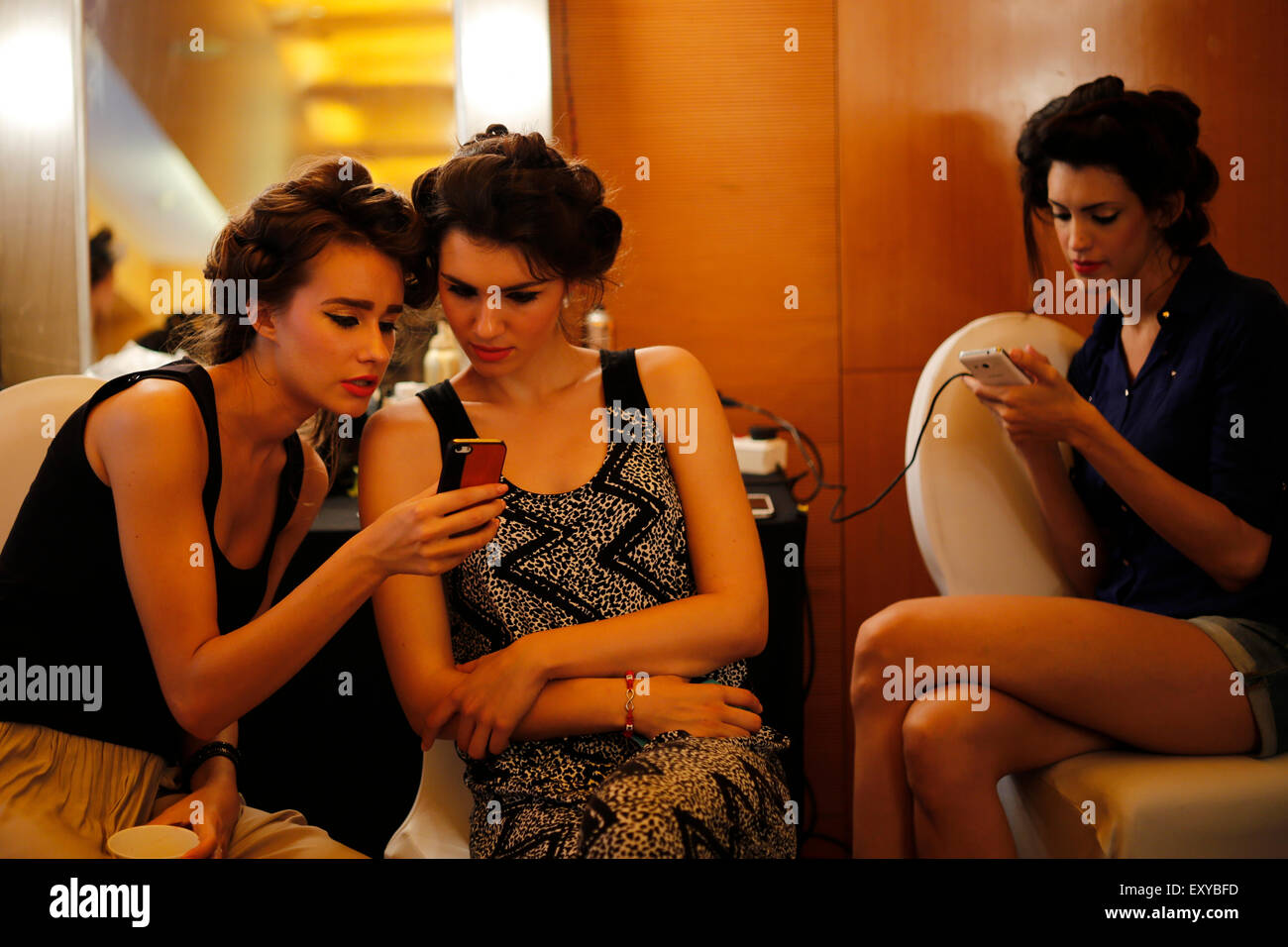 Models check their phones in the makeup room backstage before fashion show Stock Photo