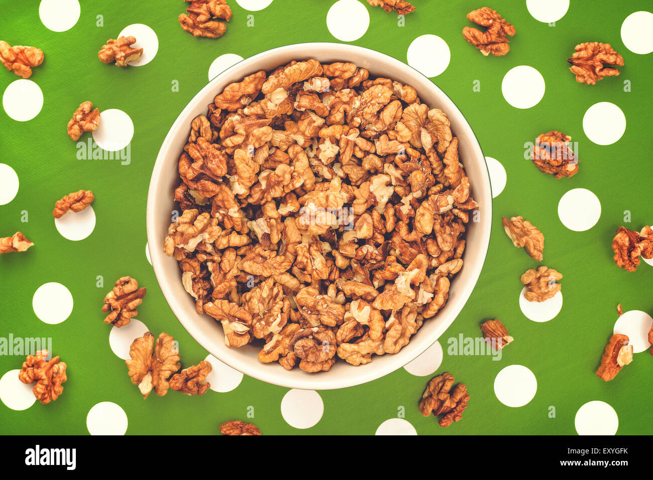 Peeled Walnut Kernels in Ceramic Bowl on Green Polka Dotted Background, Top View Stock Photo