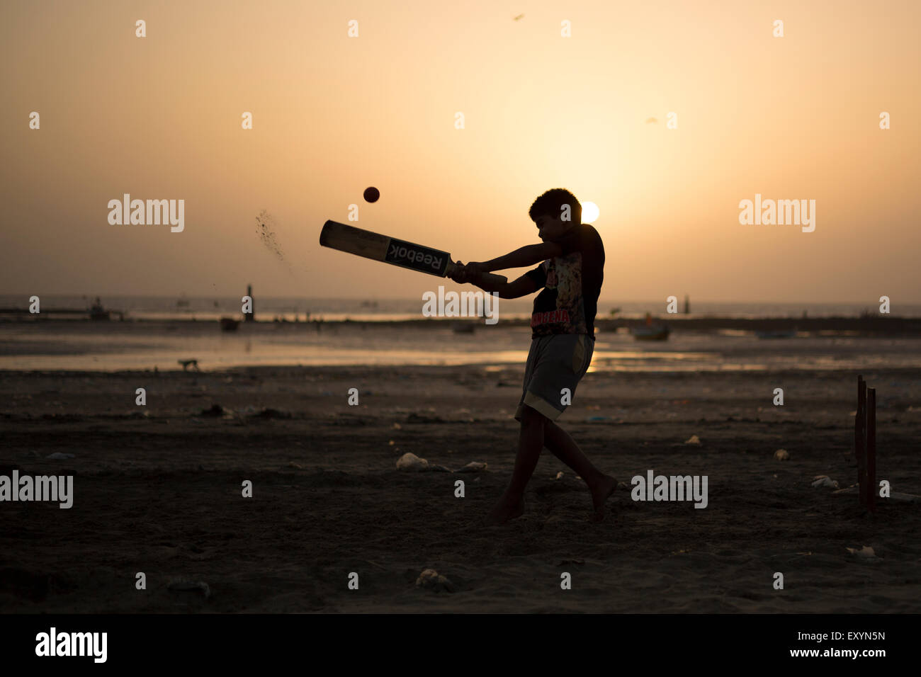 An Indian boy playing cricket during sunset at juhu beach in Mumbai, India. Stock Photo