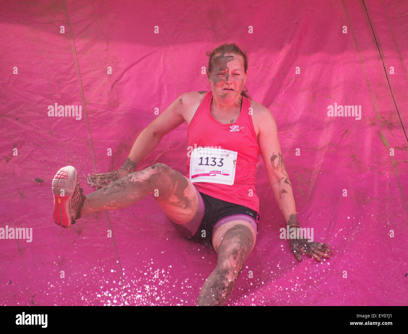 Portsmouth, UK. 18th July, 2015. A participant in the Race For Life - Pretty muddy slides down a water covered slide towards a pit of mud. The Race for Life Pretty Muddy event is open to females only and consists of a 5K mud covered obstacle course Credit:  simon evans/Alamy Live News Stock Photo