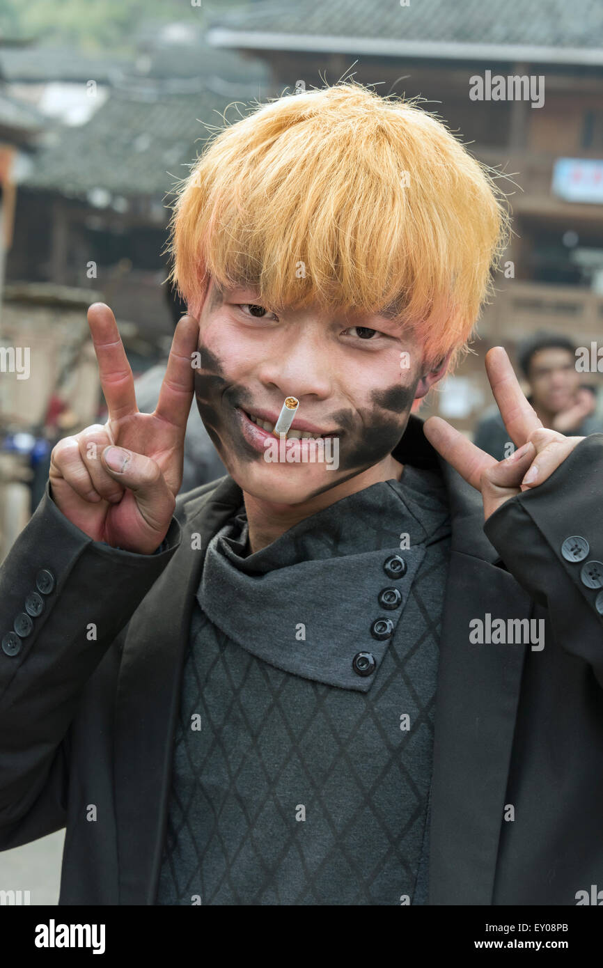 Bleached blond Dong youth covered with firecracker soot, making peace sign, Huanggang Dong Village, Guizhou Province, China Stock Photo