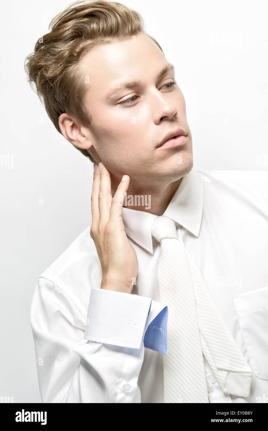 A handsome young man, male model, wearing a white shirt with white necktie, posing. A high fashion editorial concept. Stock Photo