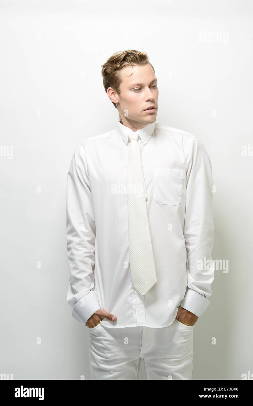 A blond, handsome man, male model, standing, posing in an all white outfit, a futuristic fashion concept. Stock Photo