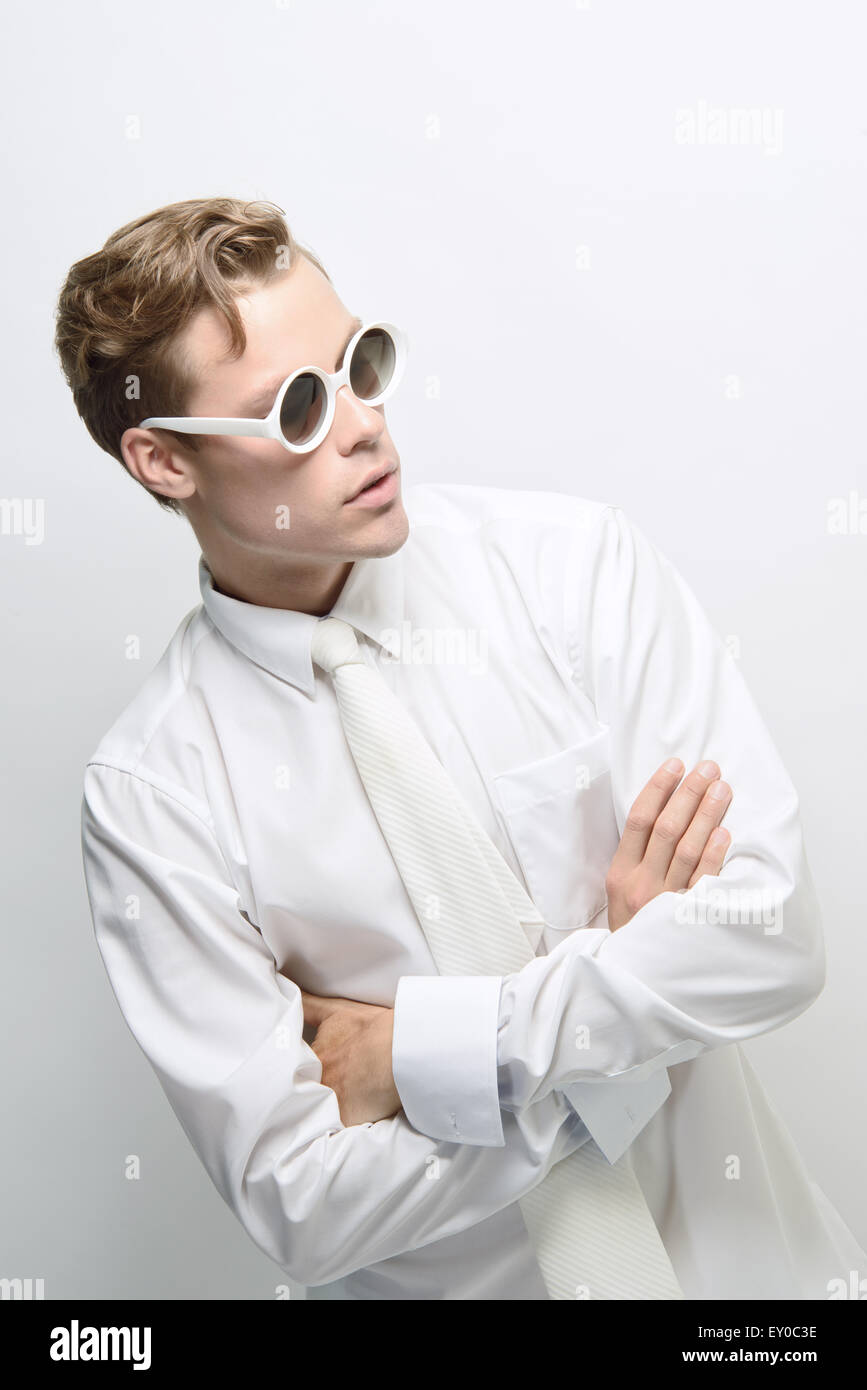 A young man, male model, wearing an all white outfit and round sunglasses posing. A futuristic concept, high fashion concept. Stock Photo