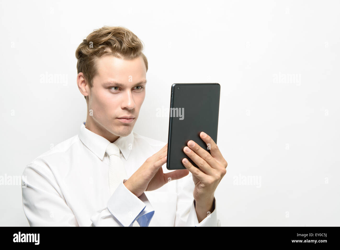 A handsome young man using an ipad/tablet. He wears an all white outfit, a clean futuristic concept. Stock Photo