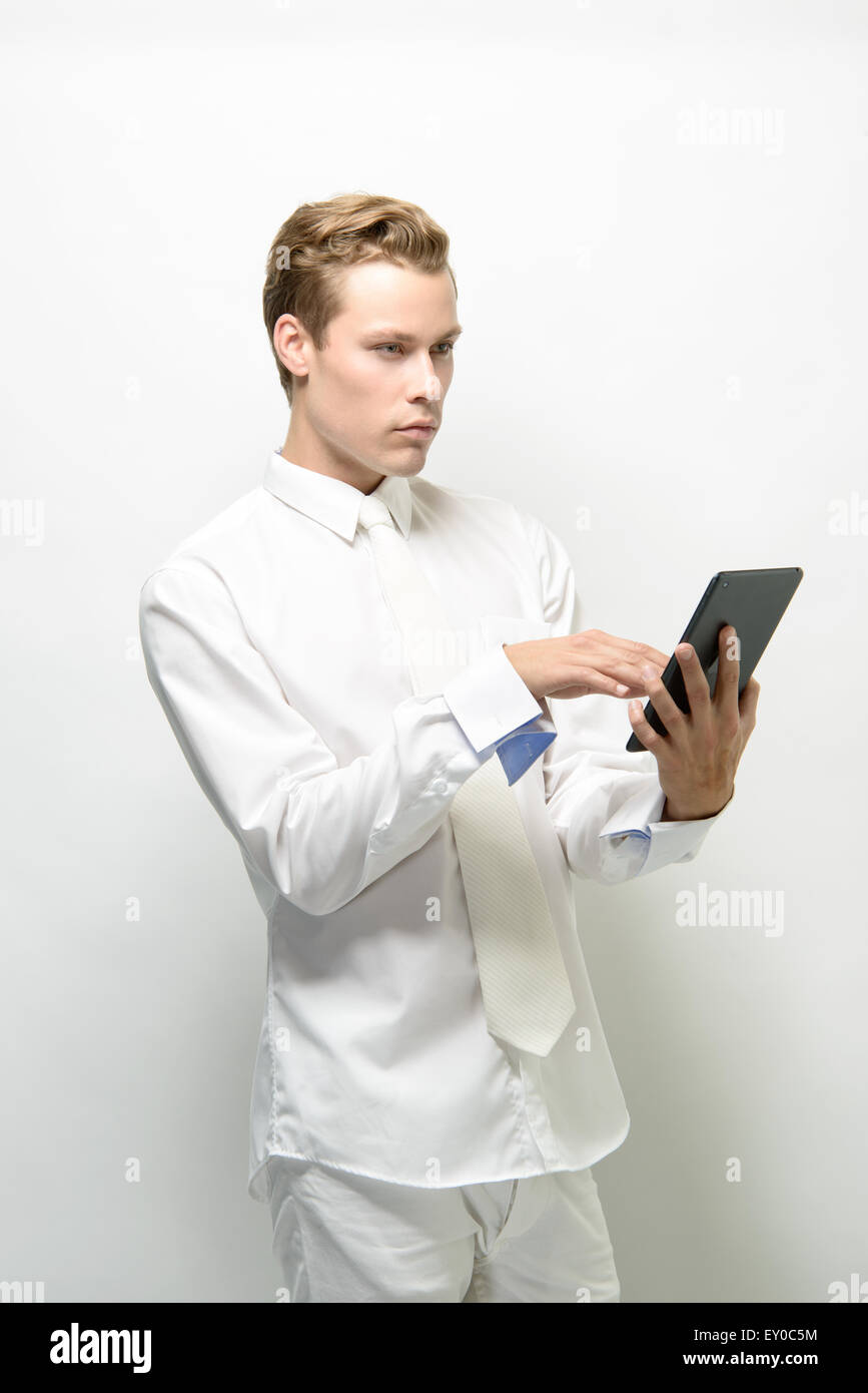 A handsome young man holding an ipad/tablet, looking away. He wears an all white outfit, a  clean futuristic concept Stock Photo