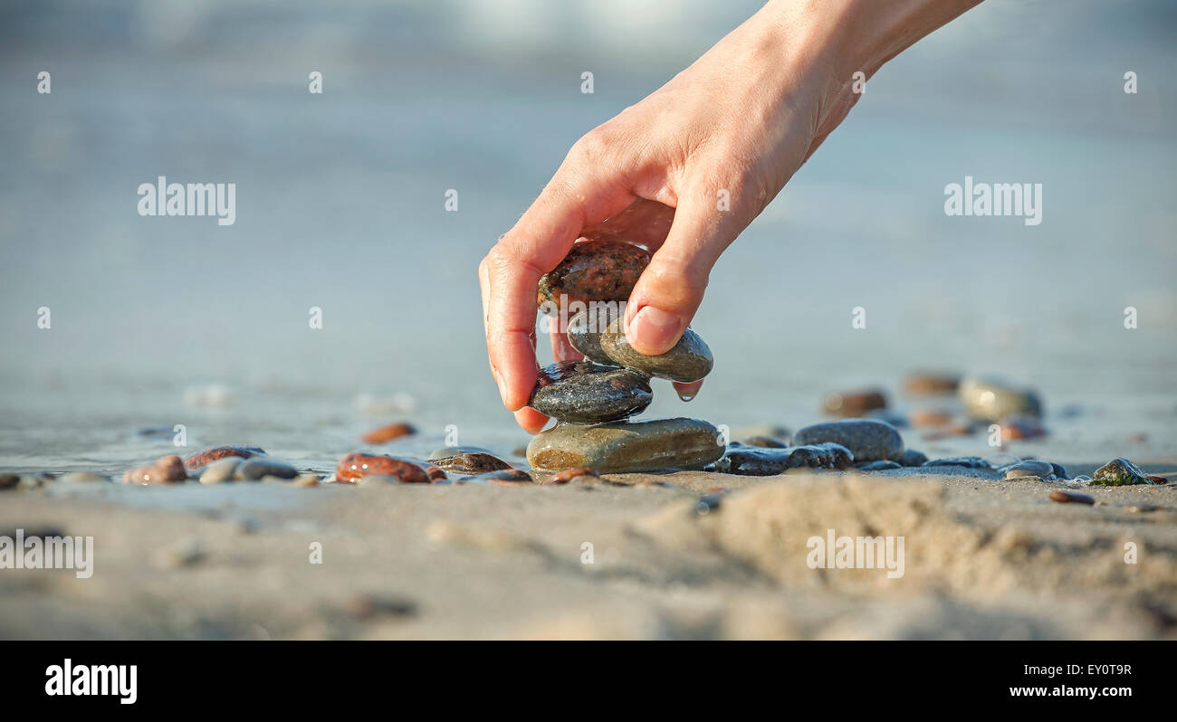 Hand arranging stone stack on beach, concept of balance and harmony. Stock Photo