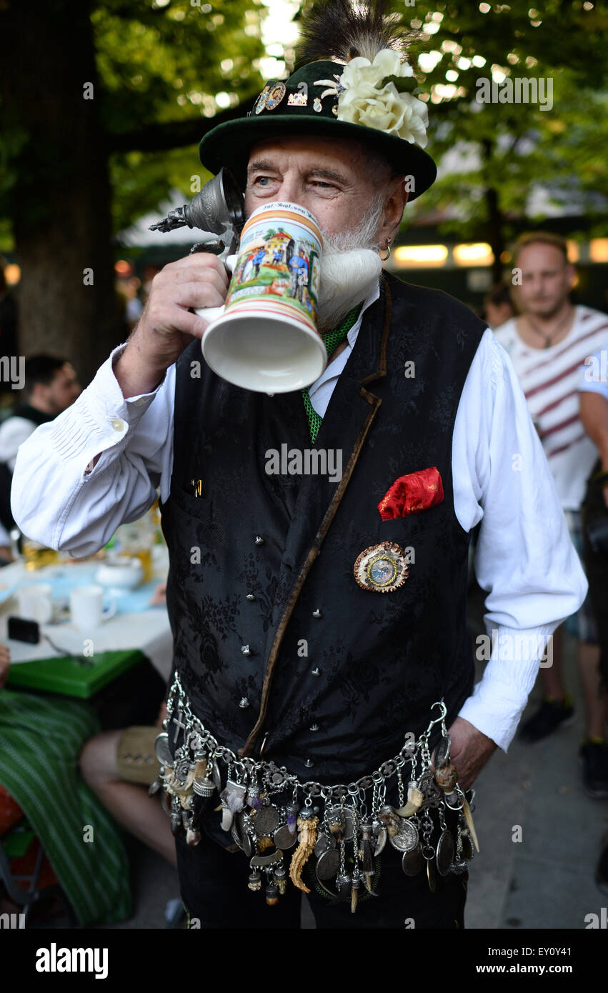 Munich, Germany. 19th July, 2015. A man dressed dressed in traditional Bavarian cloths drinks from a pint of beer in the beer garden of the 'Englische Garten' park during the Traditional 'Kocherlball' event in Munich, Germany, 19 July 2015. The Kocherlball is an old local event which referse to a 19th century tradition when servants, cooks, errand boys, nursemaids and house servants came together, on warm and sunny summer days, to spend some leisurely time with dancing and drinking at the 'Englische Garten'. Photo: Andreas Gebert/dpa/Alamy Live News Stock Photo