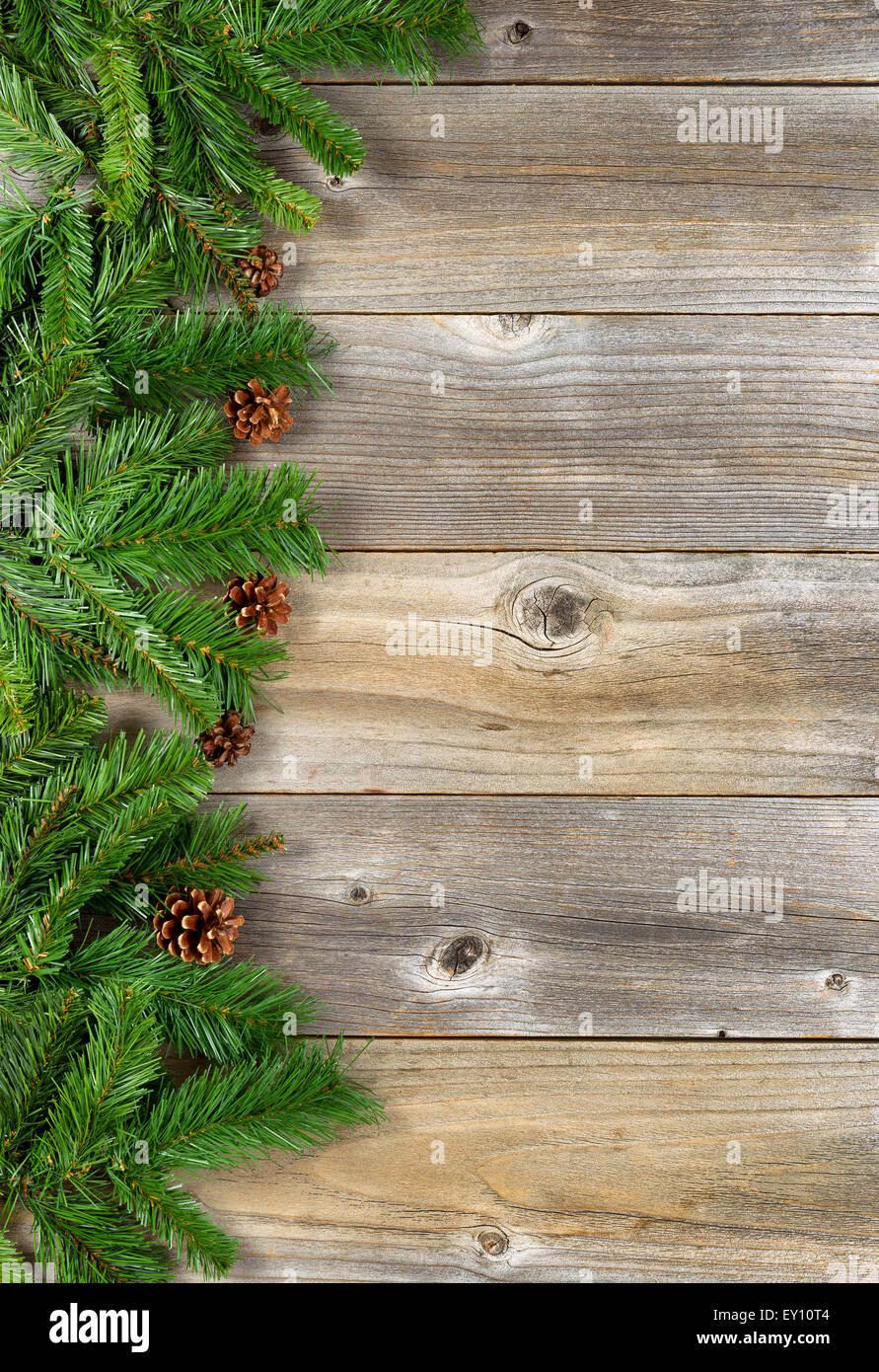 Christmas border with pine tree branches, and cones on rustic wooden boards. Layout in vertical format. Stock Photo