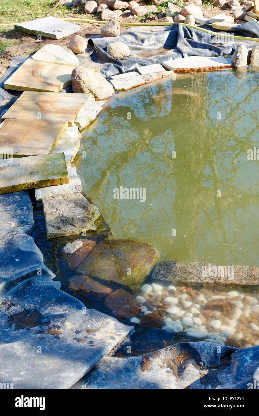 Sandstone plates, rocks and pebbles arranges around the edge of a pond. Stock Photo