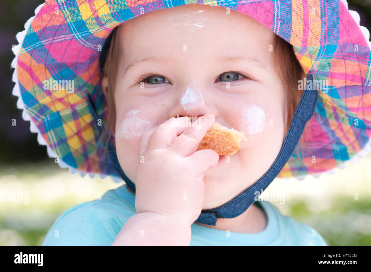 Portrait of a little girl wearing a sun hat eating bread with sun cream