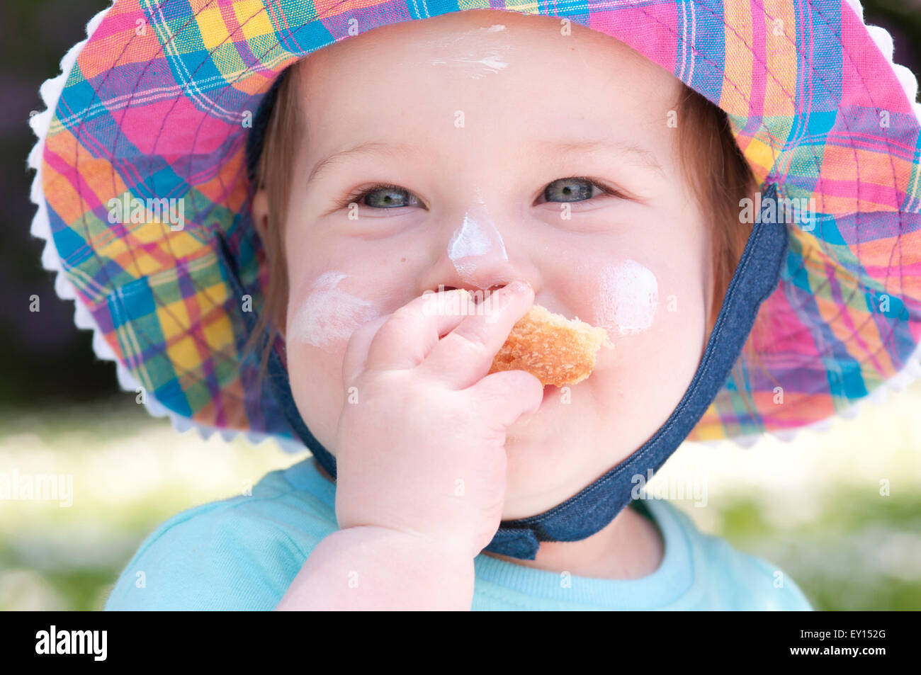 Portrait of a little girl wearing a sun hat eating bread with sun cream on her face Stock Photo