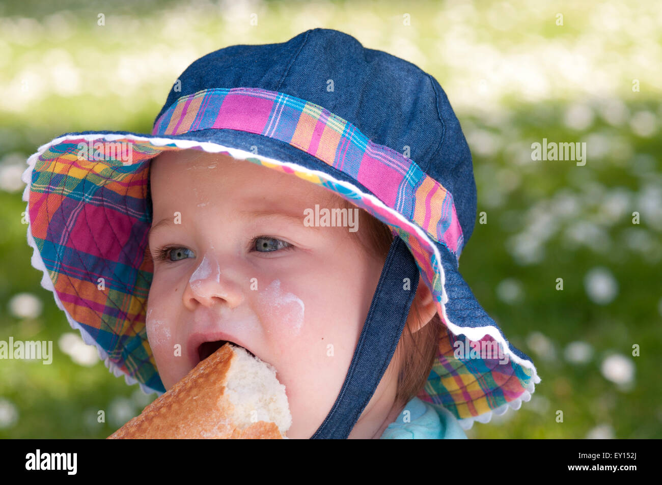 Portrait of a little girl wearing a sun hat outdoors eating bread Stock