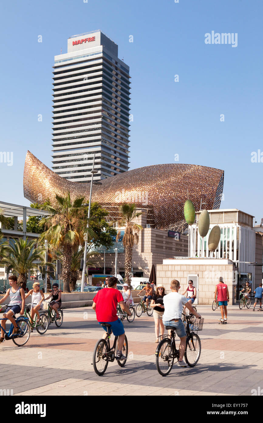 People cycling along the Passeig Maritim, with fish sculpture in the background, Barceloneta, Barcelona Spain Europe Stock Photo