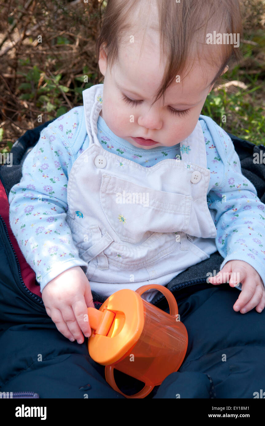 Baby girl sitting up unaided playing with her trainer cup Stock Photo
