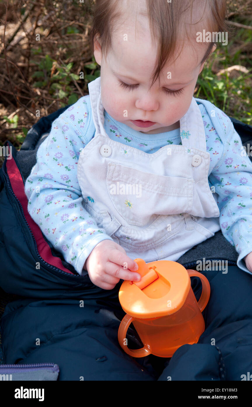 Baby girl sitting up unaided playing with her trainer cup Stock Photo