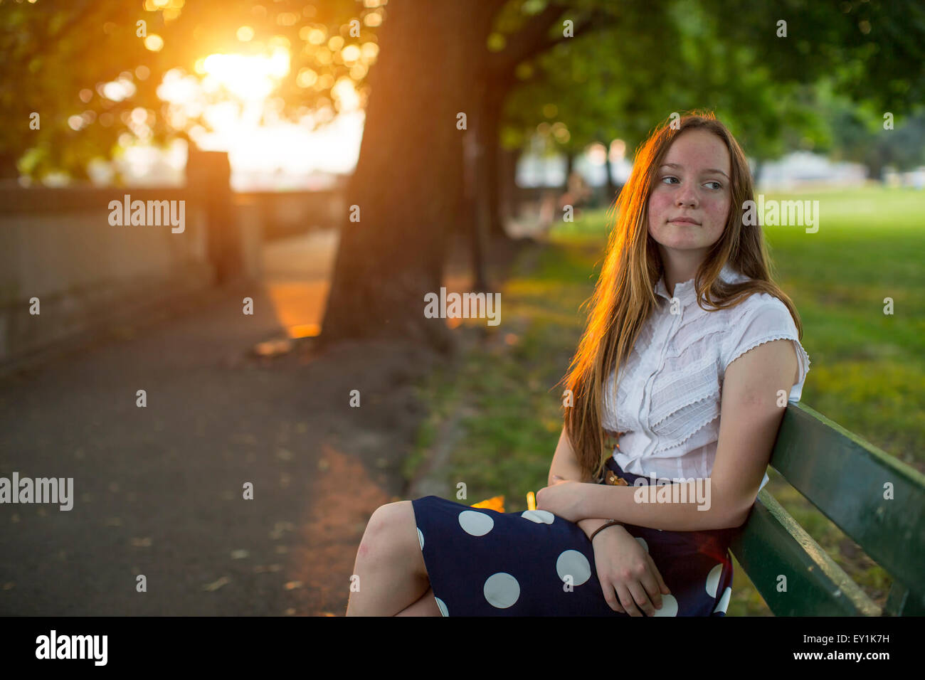 Beautiful young long haired girl sitting in a Park during golden sunset. Stock Photo