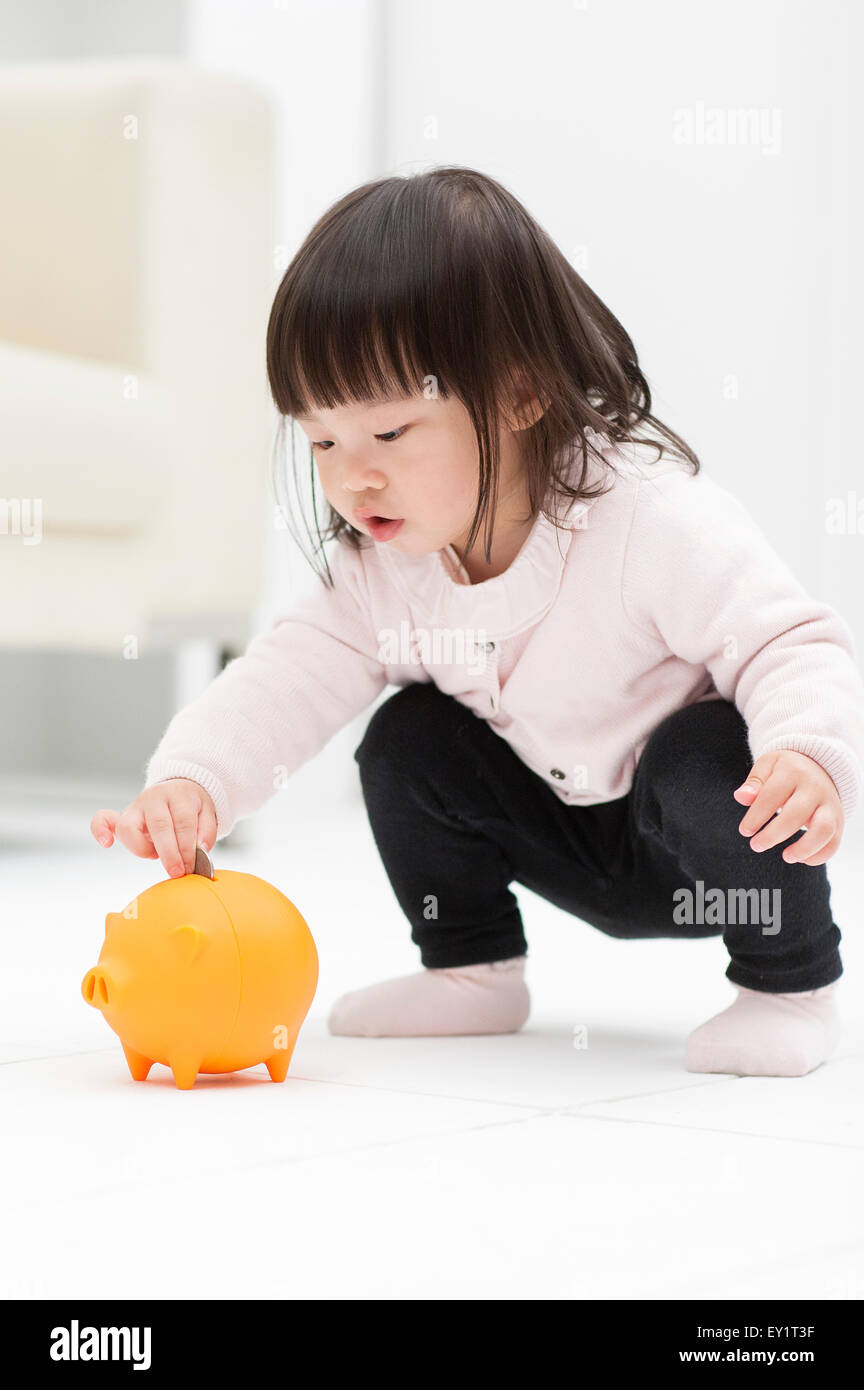 Baby girl putting coin into piggy bank Stock Photo - Alamy