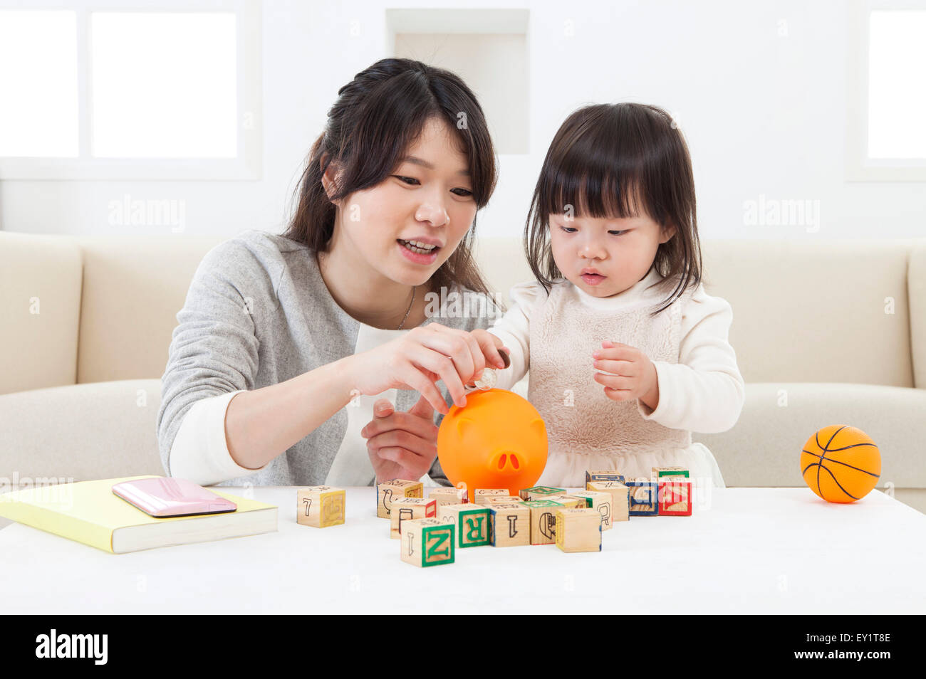 Mother and baby girl holding piggy bank and looking down Stock Photo ...