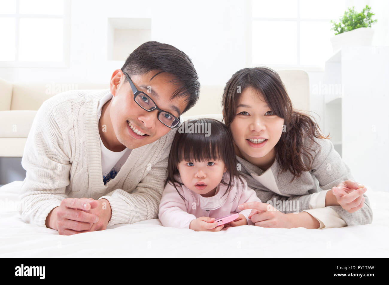 Family with one child lying down on front and smiling at the camera together, Stock Photo
