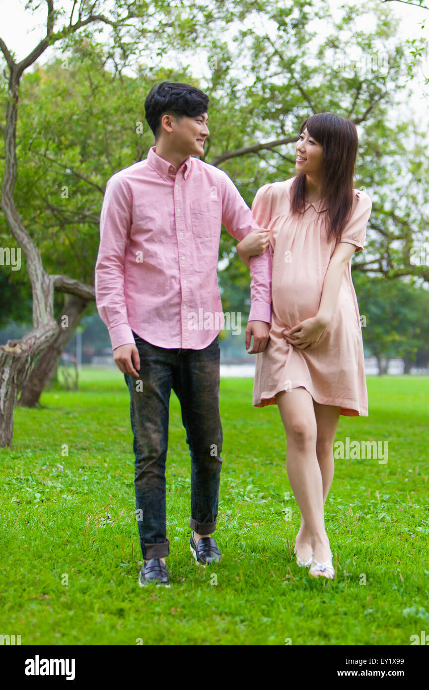 Young man and pregnant woman walking on the lawn and looking away with smile, Stock Photo