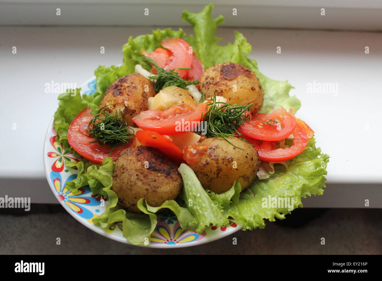 appetizing young potato made on grill lay on green leaves of salad with slices of red pulp tomato and dill Stock Photo