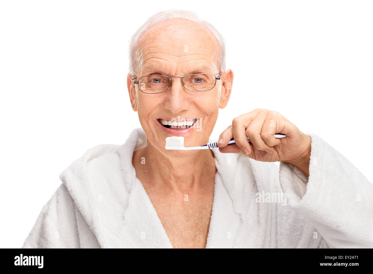Studio shot of a cheerful senior in a white bathrobe brushing his teeth and looking at the camera isolated on white background Stock Photo