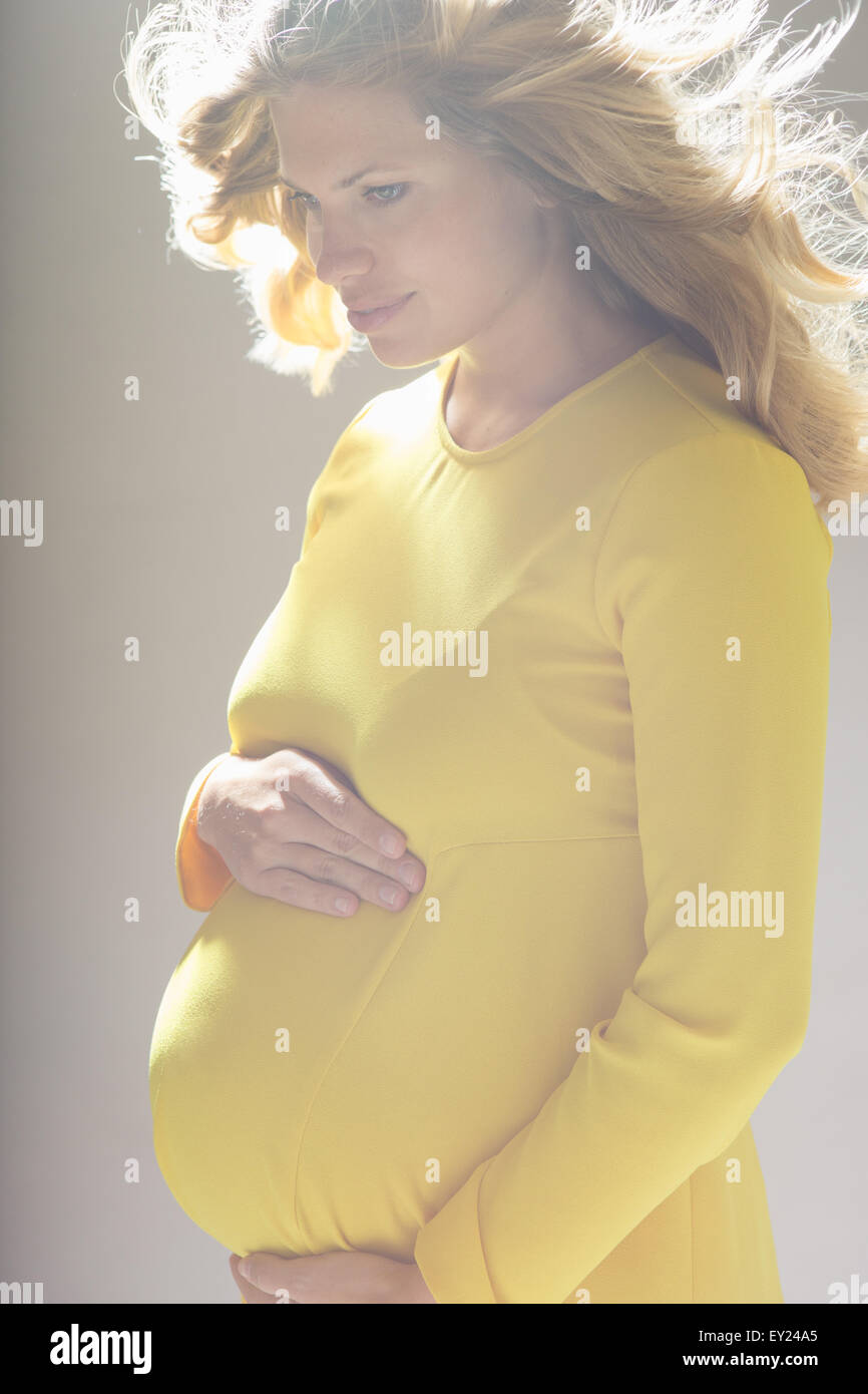 Studio portrait of pregnant young woman looking down whilst holding stomach Stock Photo