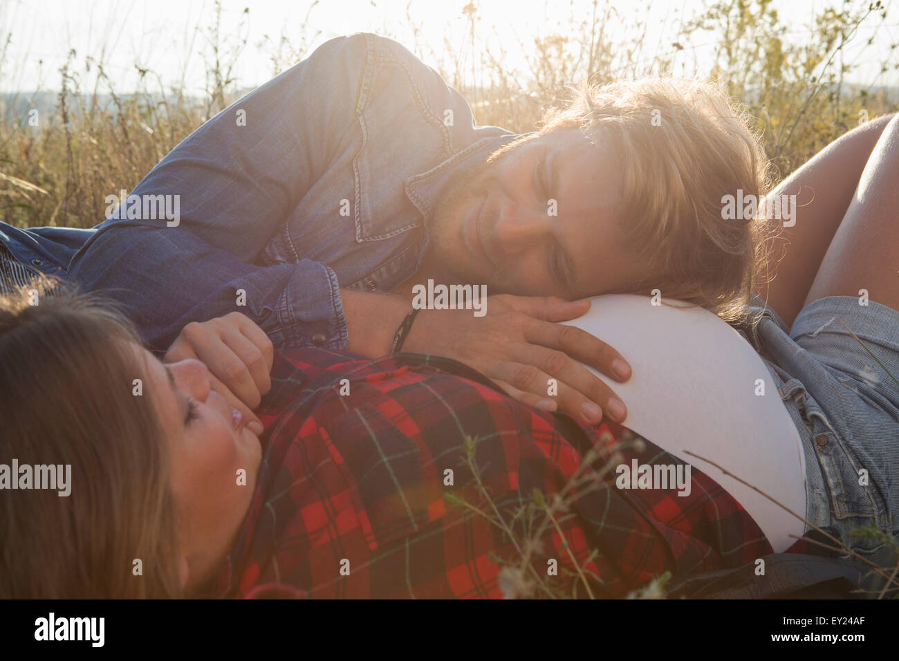 Young man listening to pregnant girlfriends stomach in field Stock Photo