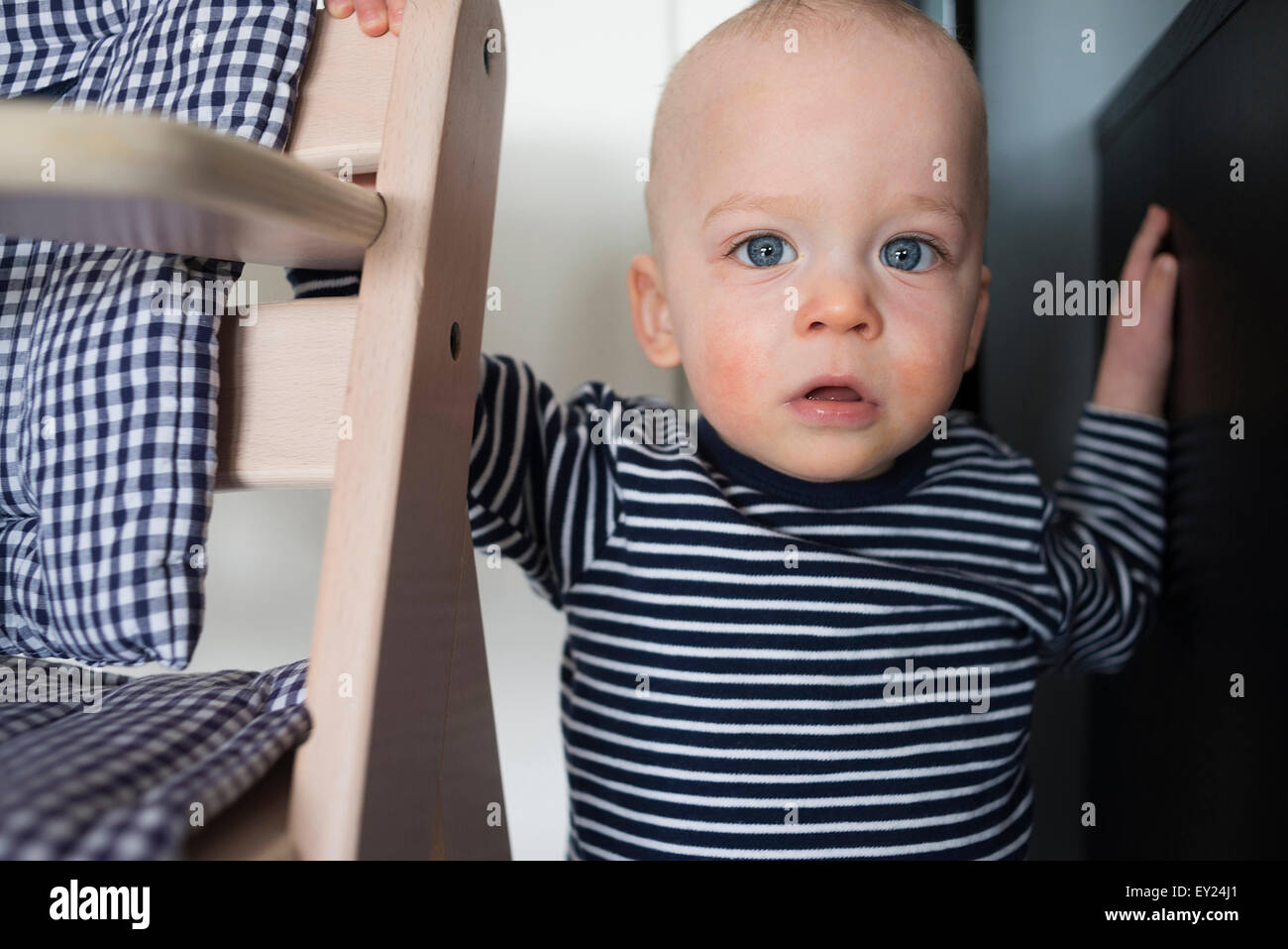 Portrait of staring baby boy next to high chair Stock Photo