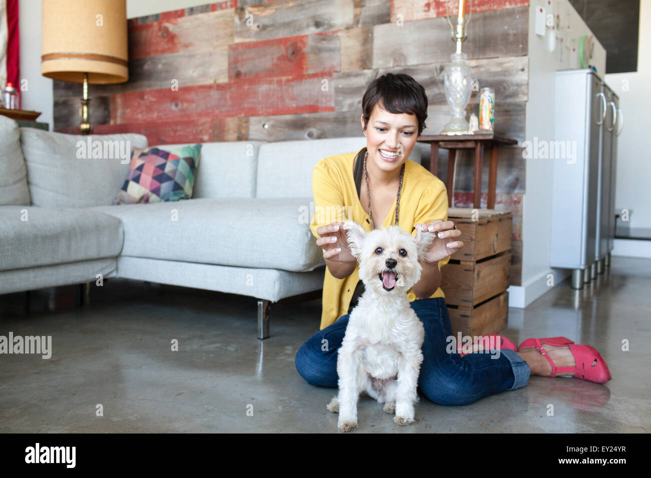 Young woman holding up dogs ears in living room Stock Photo