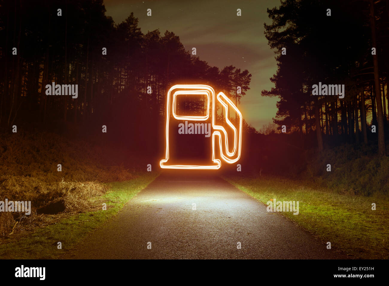 Glowing gas pump symbol above forest road at night Stock Photo