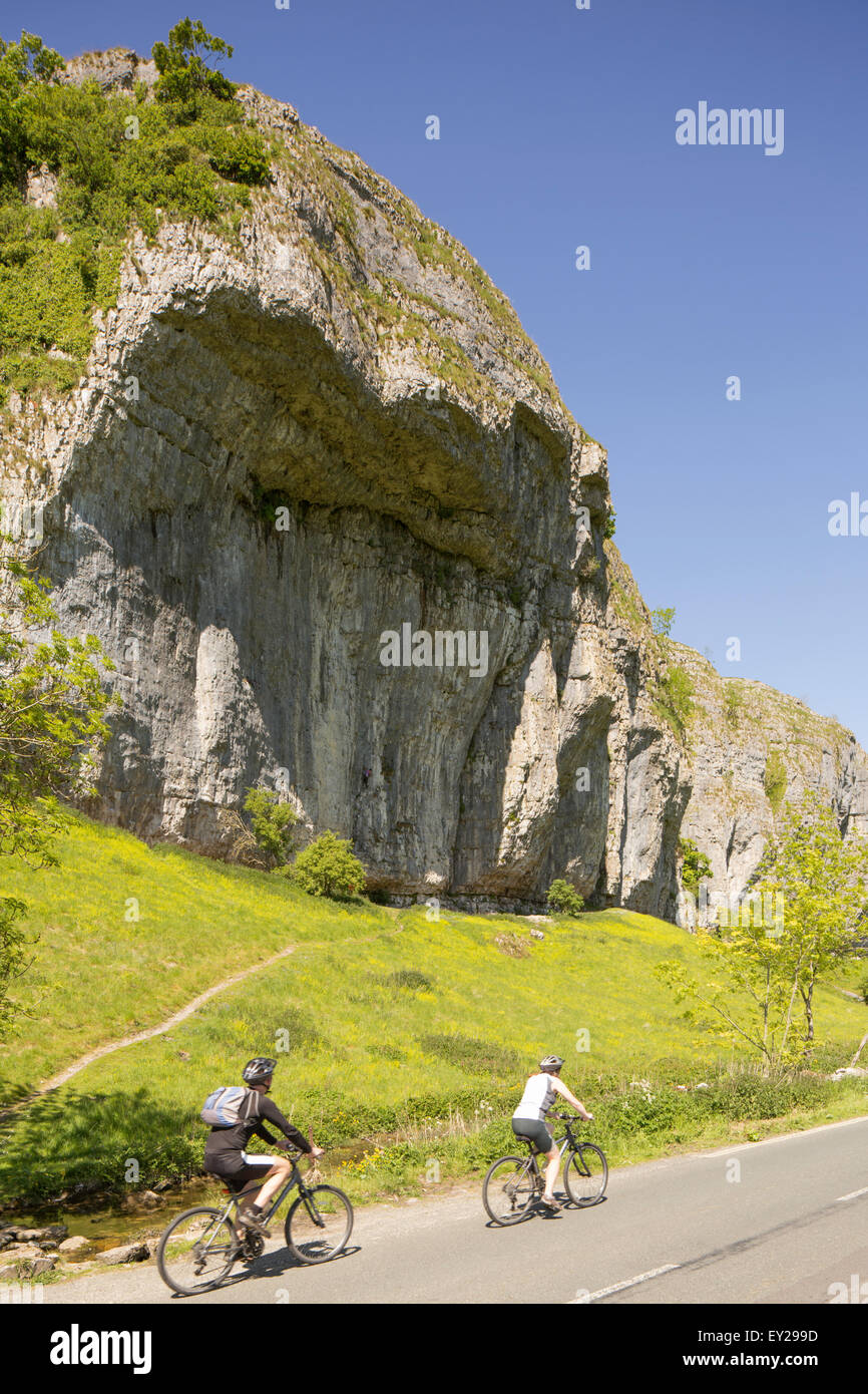 Cyclists passing Kilnsey Crag, Wharfedale, Yorkshire Dales National Park. North Yorkshire, England, UK Stock Photo