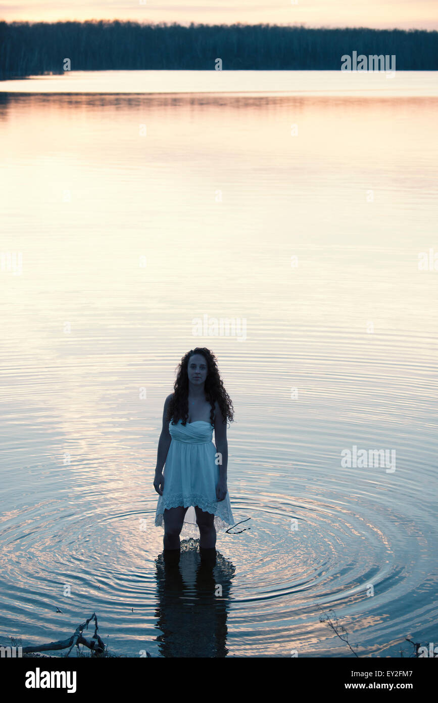 A woman in a white dress in shallow water at dusk Stock Photo