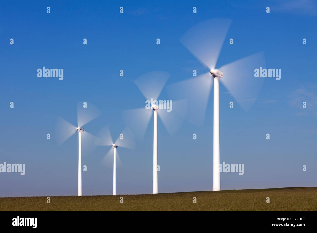Spinning rotor blades of wind turbines at windf arm against blue sky