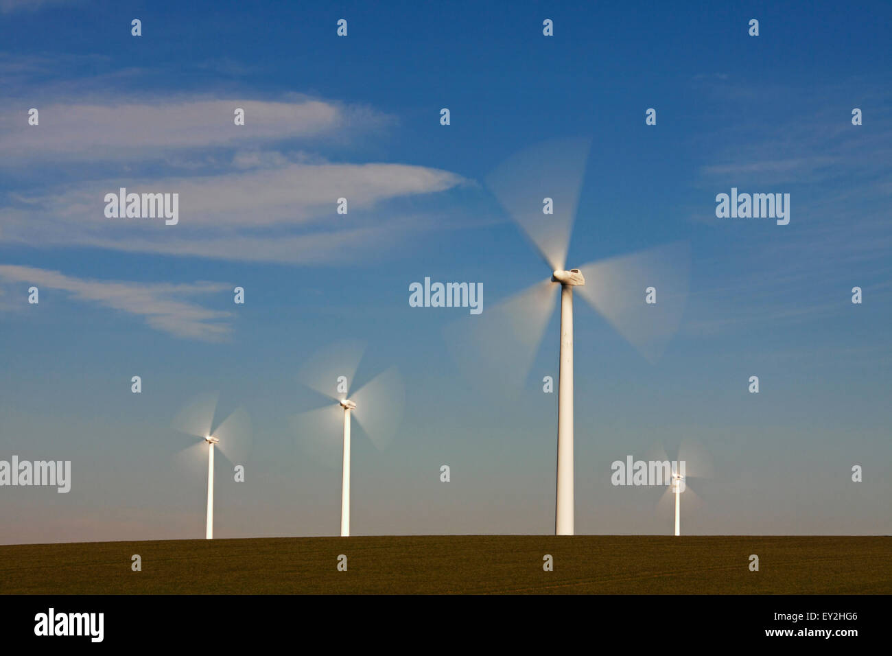 Spinning blades of wind turbines at wind farm against blue sky Stock